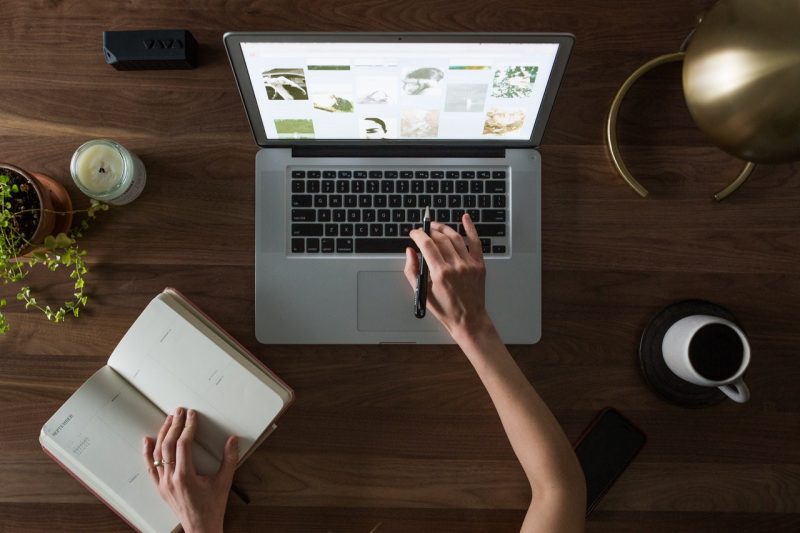 A person sitting at a laptop with a notebook.