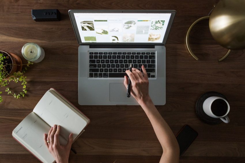 A person sitting at a laptop with a notebook.