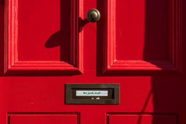 A red door with a sign over the mail slot reading "no junk mail".
