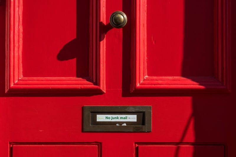 A red door with a sign over the mail slot reading "no junk mail".