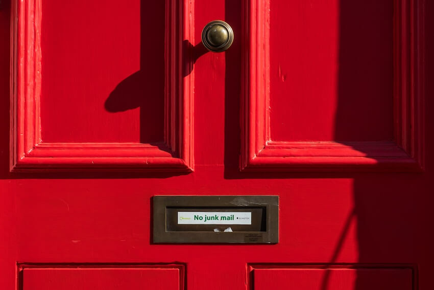 A red door with a sign over the mail slot reading "no junk mail".