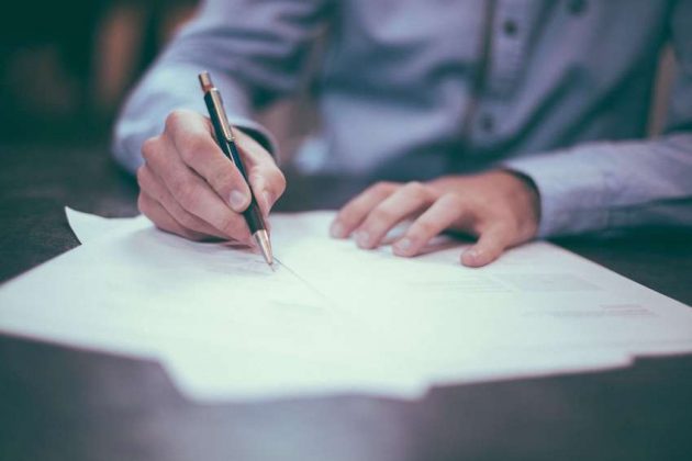 A man writing on a piece of paper with a pen.